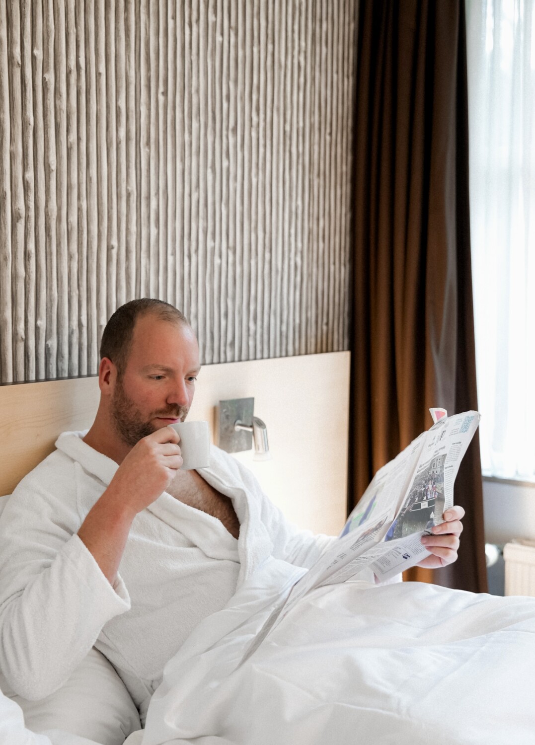 Man in bed geniet van koffie bij Buitengoed Fredeshiem Solo genieten van de luxe bij Buitengoed Fredeshiem